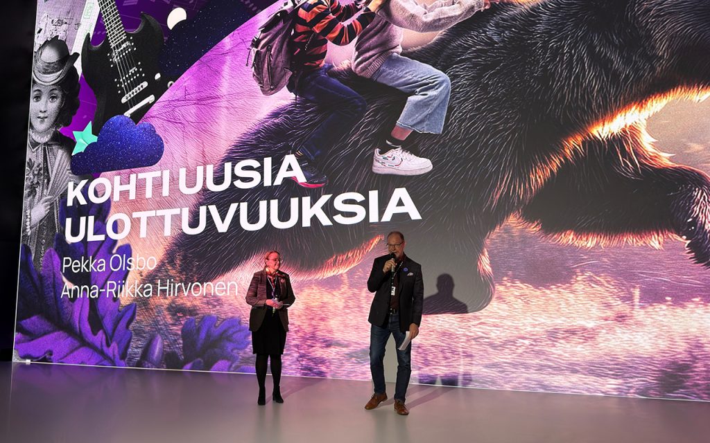 Nainen ja mies puhuvat valtavan näyttöseinän edessä.