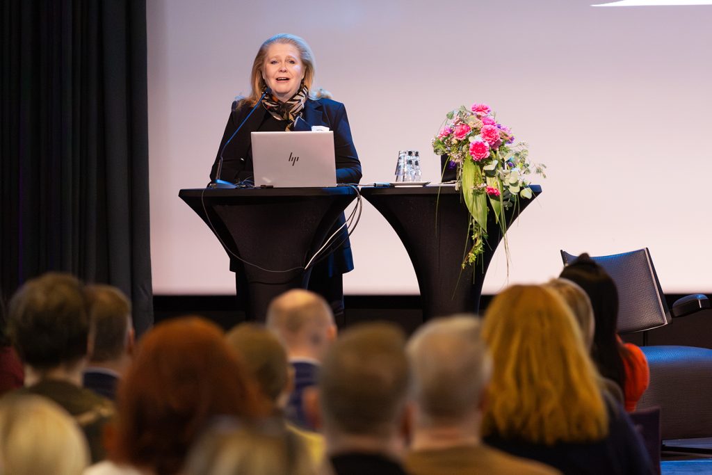 Nainen puhujapöntössä puhuu yleisön edessä.